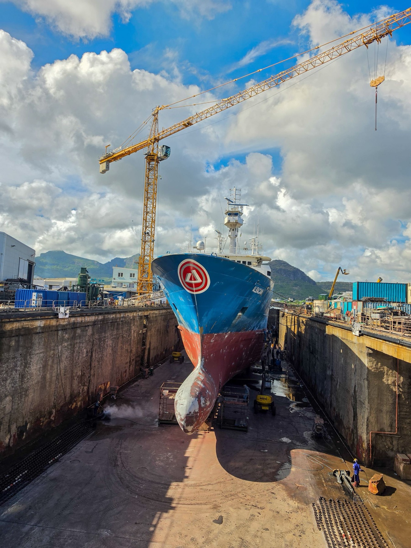 Commercial vessel in dry dock at a shipyard with crane and maintenance workers